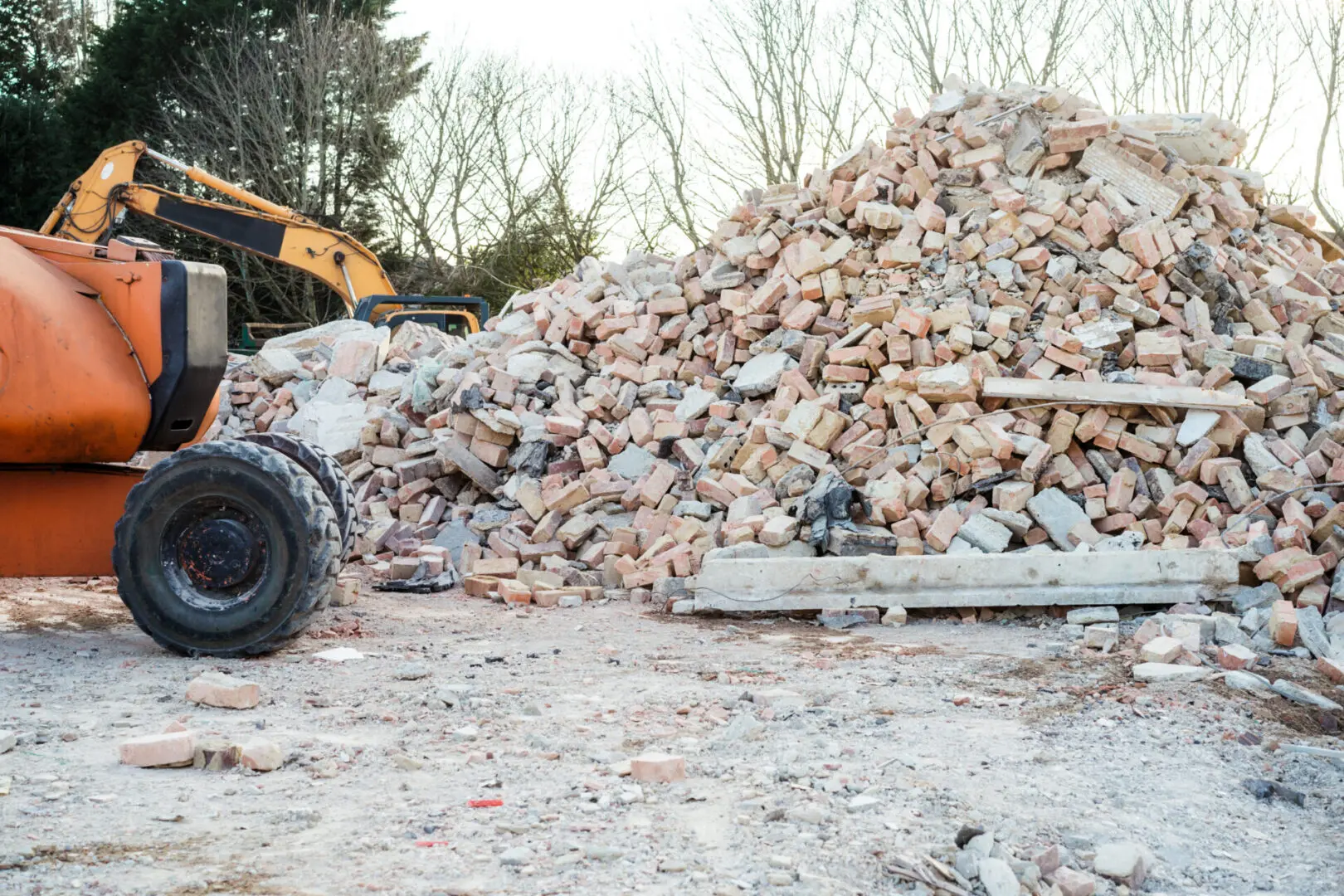 Pile of broken bricks and debris with a construction vehicle in the background at a demolition site.